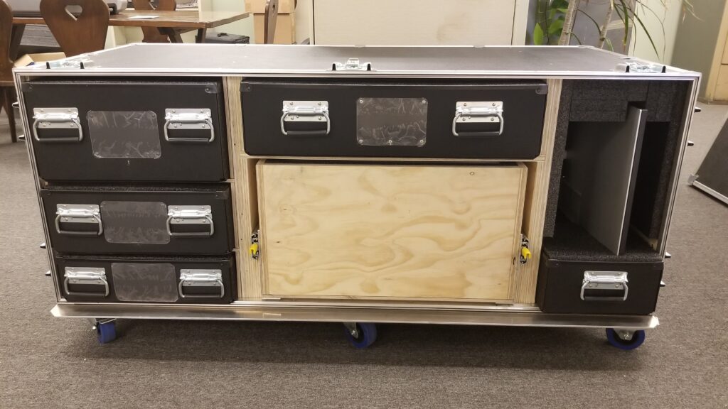 Large custom rolling equipment case with multiple drawers, reinforced handles, wheels, and open storage compartments for tools and equipment.